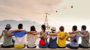a group of young friends with arms around each other's shoulders, seen from behind, sitting near a cable car