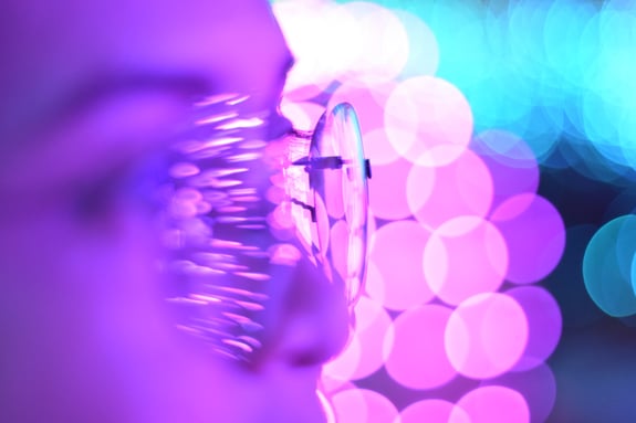 Decorative image of a person wearing eyeglasses, lit by bright purple and turquoise lights